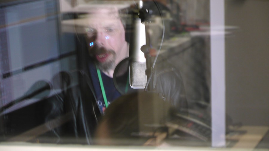 a blurred image taken through glass of Jez singing in a sound booth with a mic in front of him