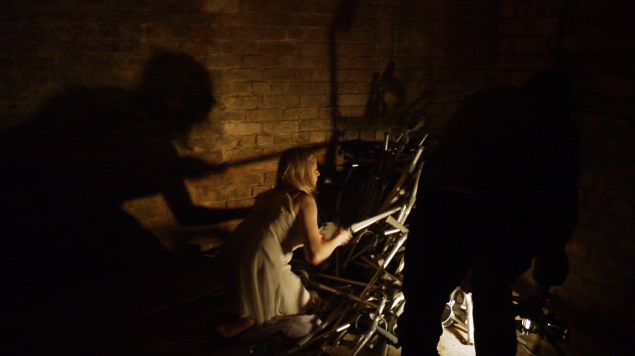 claire is kneeling on the floor, in profile, searching through a large pile of crutches.
