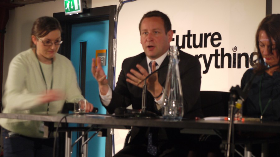 Ed Vaizey, Minster for Culture, Communications and Creative Industries at DCMS sitting at a table speaking animatedly - there is a sign behind him, just readable, which says Future Everything.
