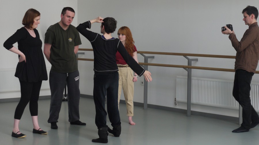 Janice Parker talks to three dancers and demonstrated a stretch in a dance rehearsal room.