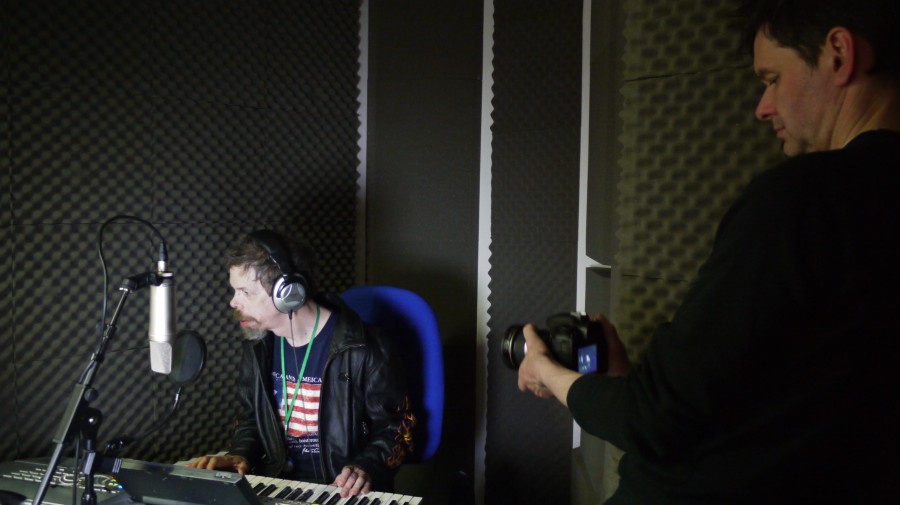 Jez on keyboard with earphones in a recording studio - being filmed by a camera man