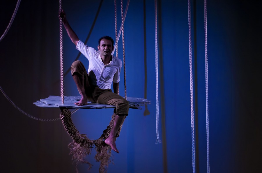 Ramesh on a suspended platform surrounded by ropes, looks out. It is dark, the background is night blue