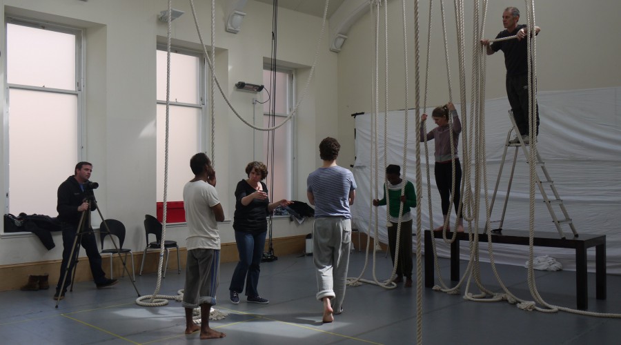 A rehearsal room hung with ropes. Three actors are by the ropes at different heights (one on a table) - Ramesh, a sign interpreter and the director look on.