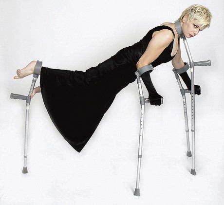 Claire Cunningham balancing on four crutches - two for her arms, one for her legs and one at her neck. She is all in black including with black long gloves.