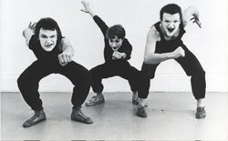 Three white faced mimes, dressed in black, in crouched poses facing the camera