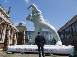 A grey inflatable, going up - you can see the legs, torso, arms and head against a blue sky. It looks like it is kneeling