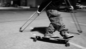 the bottom half of a man, feet on a skateboard, with crutches being used to propel the figure forwards
