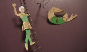 two circus figures - one on a ladder and one on a trapeze - they are made of flat metal and part of a wall hanging