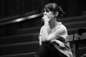 a black and white image of gail looking pensive, her hand to her mouth as she sits in an empty auditorium