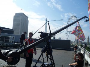 a crane with a camera at the end films jez on the roof
