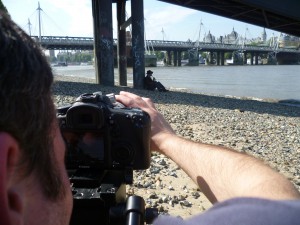 Jez sitting on the thames beach playing his whistle, being filmed
