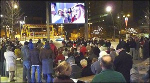 Image of the Plymouth big screen at dusk with a crowd of people gathered to watch the screen showing a band performing.